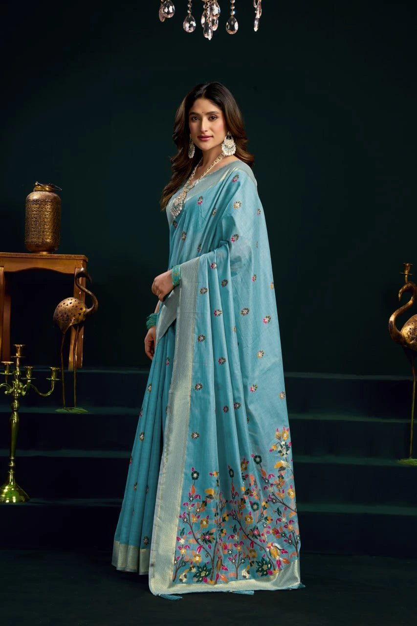 Woman wearing a light blue saree with floral patterns in a dark setting